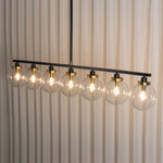 Alistair Linear Glass Globe Chandelier | Hanging Dining Room Lamp | Studio side perspective view of the 8-light linear suspension fixture illuminated against white pleated drapes | Severn Lighting