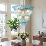 Azura Aquamarine Cascading Glass Chandelier | Glass, Metal | Staged over a minimalist dining table set with fresh flowers and surrounded by chairs next to a large potted indoor tree | Severn Lighting