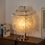 Callista Tiered Capiz Table Lamp | Capiz, Metal | Placed on a dark wood credenza console next to stacked books, creating a cozy light halo against a clean white wall | Severn Lighting