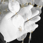 Callista Tiered Capiz Table Lamp | Capiz, Metal | Detail shot showing a white-gloved hand gently cradling the individual cascading white translucent capiz shell discs | Detail shot | Severn Lighting