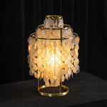 Callista Tiered Capiz Table Lamp | Capiz, Metal | Close-up staged shot of the fully illuminated capiz shell table lamp casting a heavy golden glow onto a polished dark wood table surface | Severn Lighting