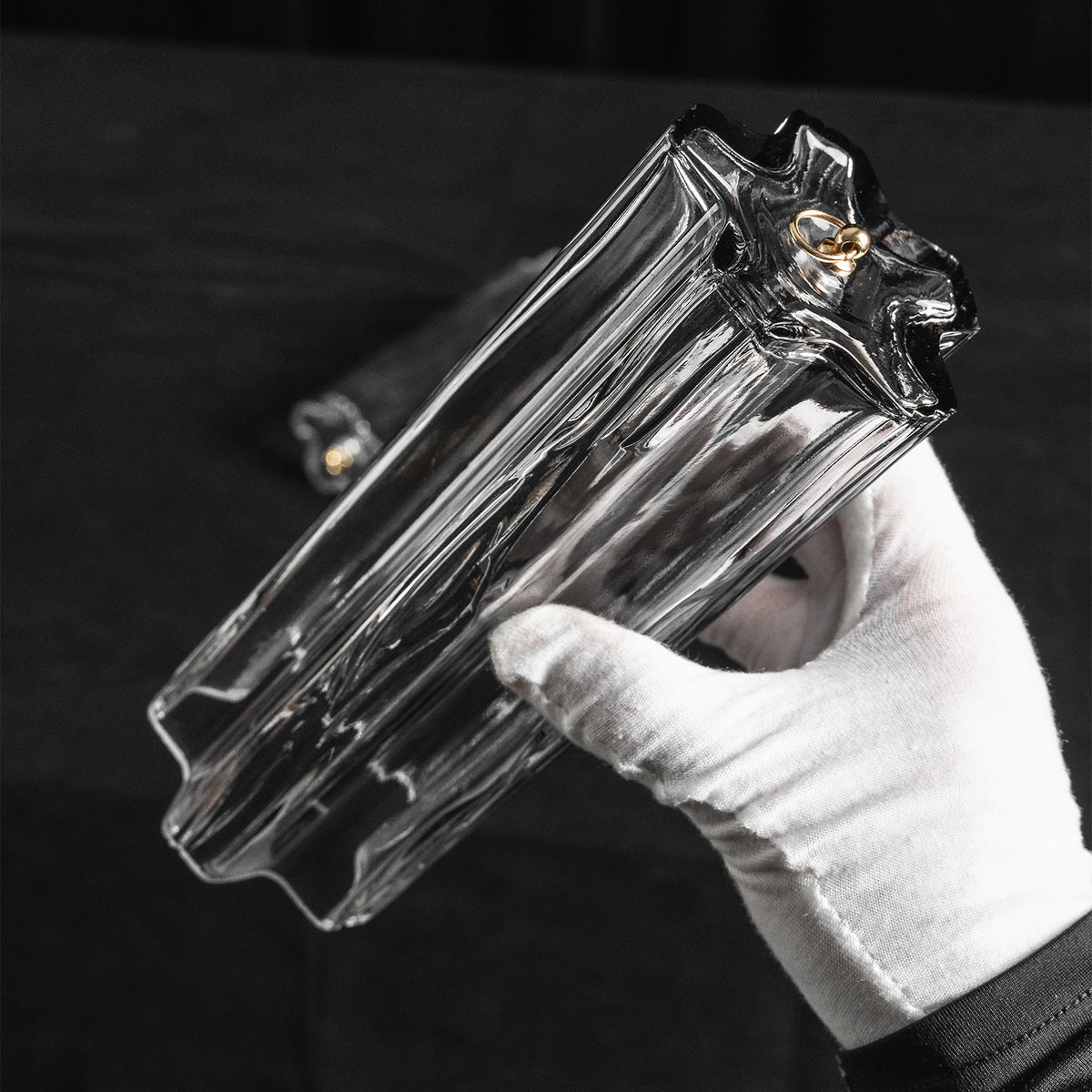 Cassian Tiered Fluted Glass Ceiling Light | Tiered Fluted Glass and Gold Brass | A hand wearing a white glove holding a single clear fluted glass rod component against a dark background | Severn Lighting