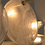 Celestia Art Glass Disc Chandelier | Glass, Metal | Close-up focus on an illuminated clear glass disc showing its organic textured surface pattern and warm light transmission | Detail shot | Severn Lighting