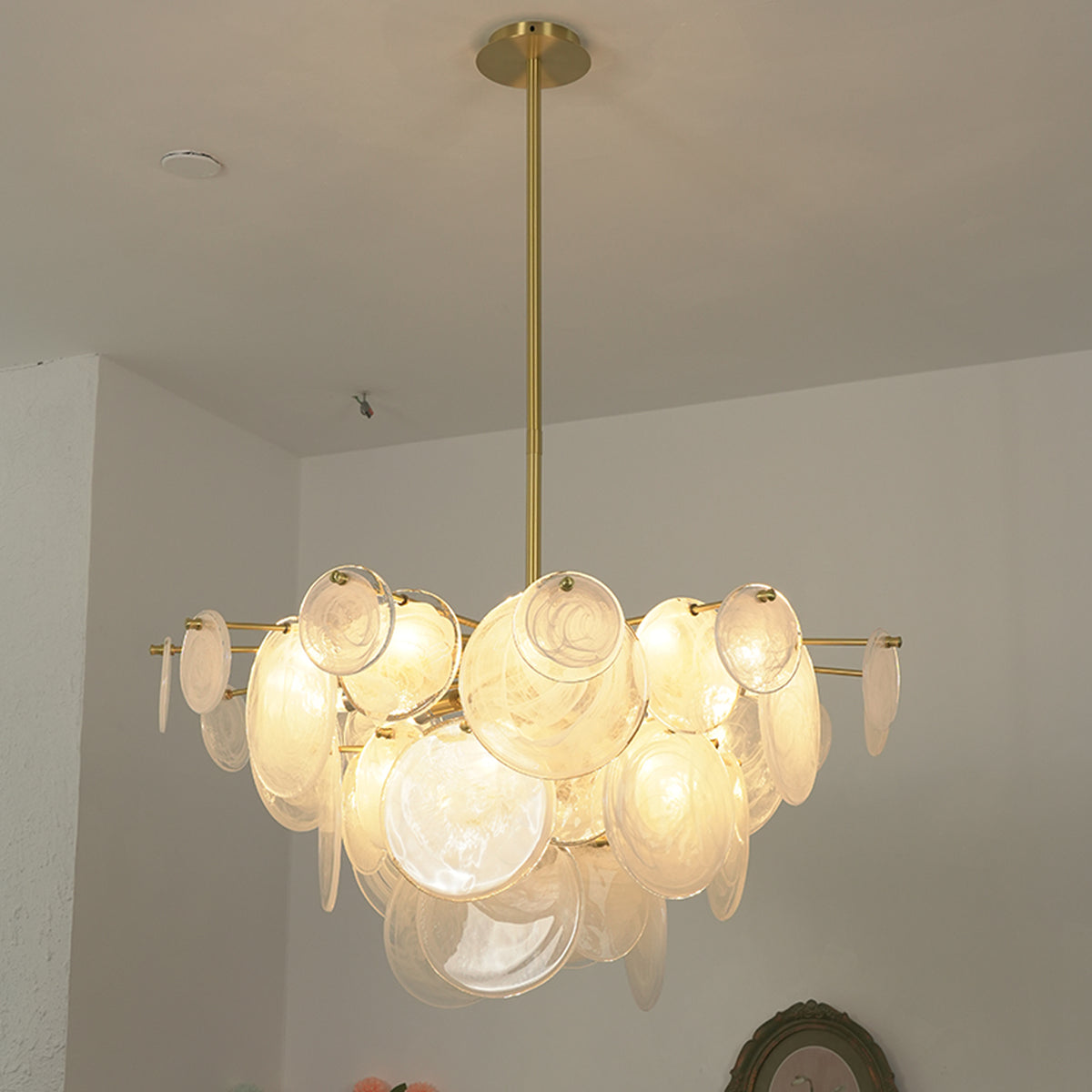 Celestia Art Glass Disc Chandelier | Glass, Metal | Studio view of the fully illuminated glass disc fixture casting a warm golden glow against a plain white wall | Severn Lighting