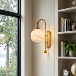 Cordelia Alabaster Globe Wall Sconce | Natural Alabaster and Brushed Brass | Styled on a slim white wall panel adjacent to a tall built-in library bookshelf | Severn Lighting