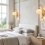 Cordelia Alabaster Globe Wall Sconce | Natural Alabaster and Brushed Brass | Installed as a pair illuminating a modern white bed setup in a bright minimalist bedroom | Severn Lighting