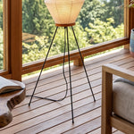 Cosima Hourglass Washi Paper Floor Lamp | Japanese Wabi-Sabi Paper and Black Tripod | Detailed view highlighting the minimal black metal tripod legs resting on a wooden deck floor | Severn Lighting