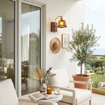 Everett Amber Ripple Wall Sconce | Amber Rippled Glass and Walnut Wood | Mounted on a balcony wall next to a glass door and an olive tree potted plant | Severn Lighting
