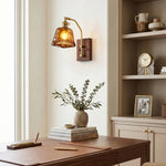 Everett Amber Ripple Wall Sconce | Amber Rippled Glass and Walnut Wood | Fixed on a home office wall casting light over a wooden desk with a built-in shelf | Severn Lighting