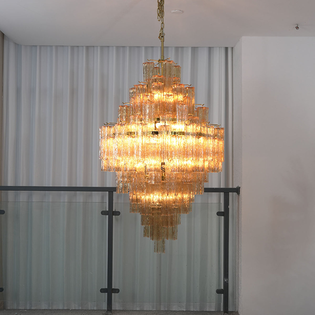 Kester Amber Glass Tier Chandelier | Amber Glass and Brass | Real-life installation view glowing warmly near a glass mezzanine railing | Severn Lighting