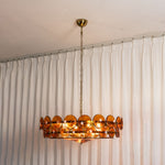 Lovenne Textured Glass Disc Ring Chandelier | Textured Glass and Brass | Real-life view of amber glass variant glowing softly near a white curtain | Severn Lighting