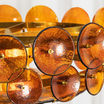 Lovenne Textured Glass Disc Ring Chandelier | Textured Glass and Brass | Close-up view of the layered amber textured glass discs glowing with warm light | Severn Lighting