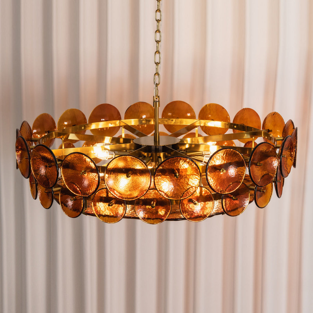 Lovenne Textured Glass Disc Ring Chandelier | Textured Glass and Brass | Amber glass variant product view hanging gracefully against striped drapes | Severn Lighting