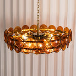 Lovenne Textured Glass Disc Ring Chandelier | Textured Glass and Brass | Amber glass variant product view hanging gracefully against striped drapes | Severn Lighting