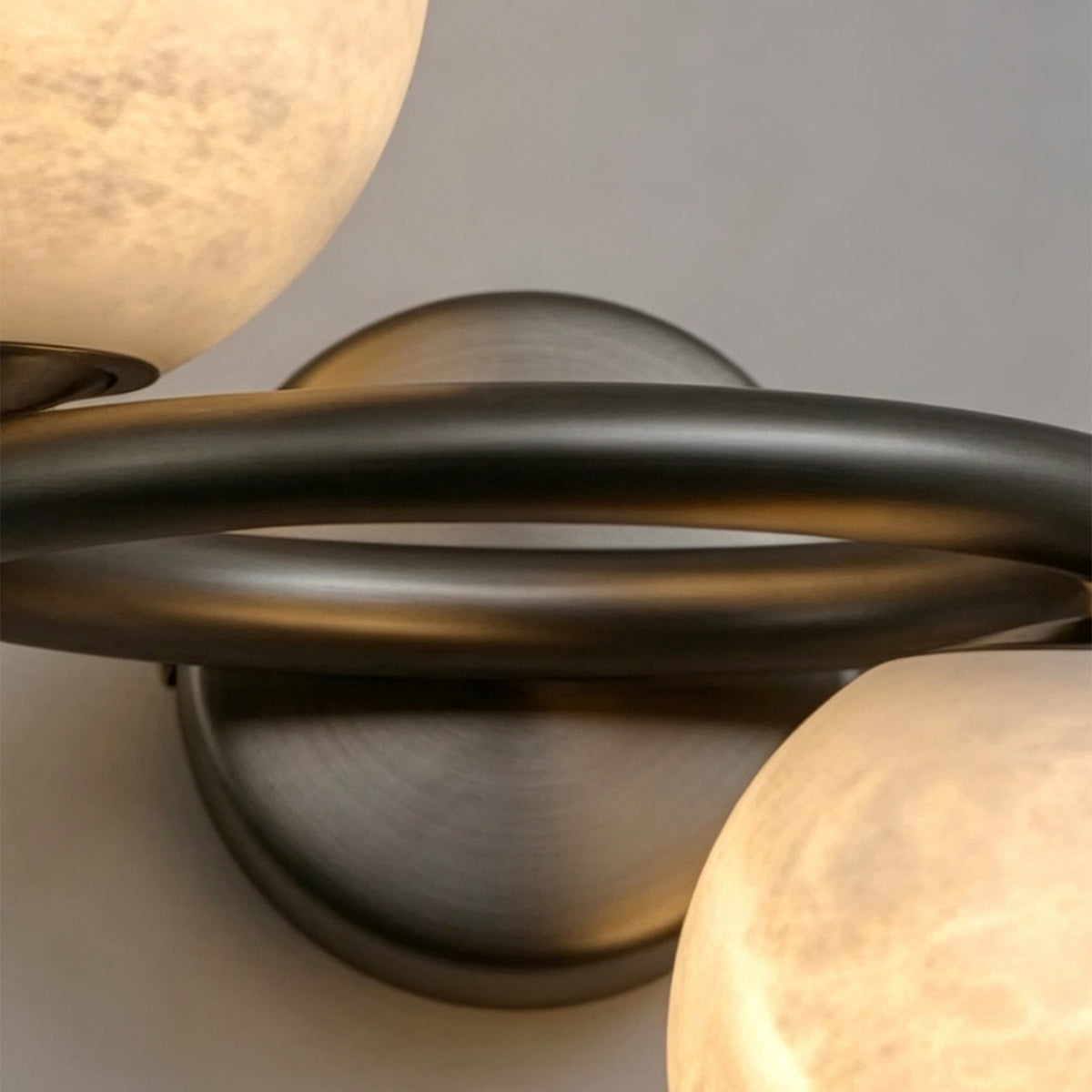 Lucern Twin Globe Alabaster Wall Sconce | Natural Alabaster and Matte Black Metal | Close-up shot focusing on the intersecting matte black loops and the circular backplate | Severn Lighting