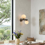 Lucern Twin Globe Alabaster Wall Sconce | Natural Alabaster and Matte Black Metal | Styled on a dining room wall near a window overlooking scenic green hills | Severn Lighting