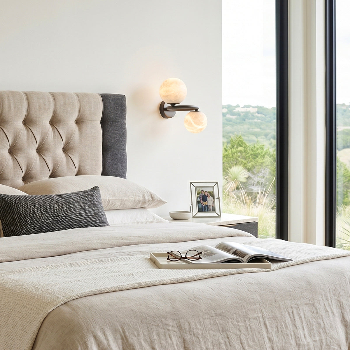 Lucern Twin Globe Alabaster Wall Sconce | Natural Alabaster and Matte Black Metal | Fixed onto a light textured bedroom wall next to a beige headboard and cozy bedding | Severn Lighting