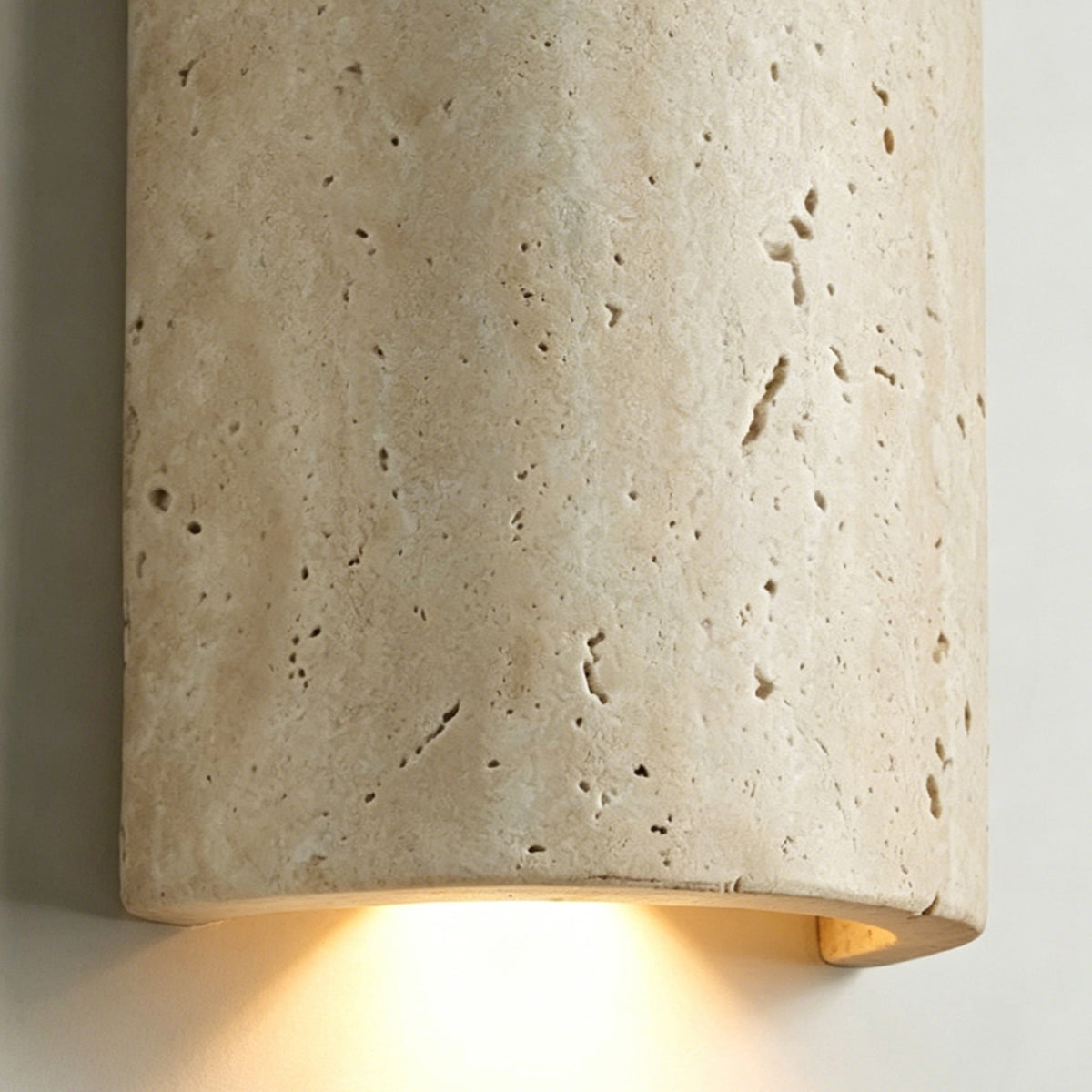 Lyra Travertine Shield Wall Lamp | Travertine, Wood, Metal | Close-up focus on the illuminated travertine wall light casting a warm golden glow from the open bottom of the shield | Detail shot | Severn Lighting