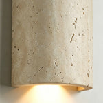 Lyra Travertine Shield Wall Lamp | Travertine, Wood, Metal | Close-up focus on the illuminated travertine wall light casting a warm golden glow from the open bottom of the shield | Detail shot | Severn Lighting