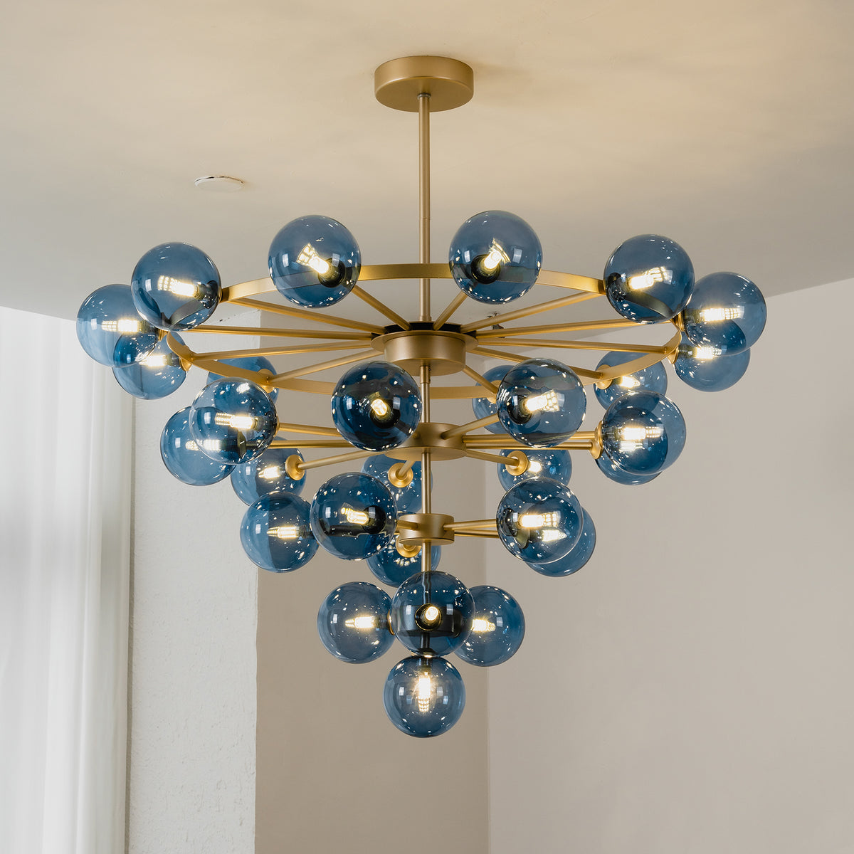 Marisol Aquamarine Glass Bubble Chandelier | Aquamarine Glass and Brass | Real-life room installation view glowing softly against a plain wall | Severn Lighting