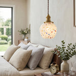Marlowe Speckled Glass Pendant Lamp | Colorful Speckled Glass and Brass | Hanging above a bed with plush pillows and a beige headboard in a contemporary bedroom | Severn Lighting