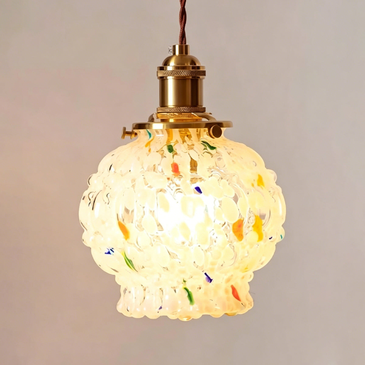 Marlowe Speckled Glass Pendant Lamp | Colorful Speckled Glass and Brass | Studio view of the single globe fixture fully lit and glowing against a light grey background | Severn Lighting