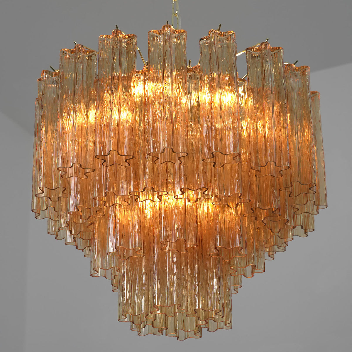 Merlande Amber Glass Tube Tiered Chandelier | Fluted Amber Glass and Brass | Full product view illuminated gracefully against a plain grey backdrop | Severn Lighting