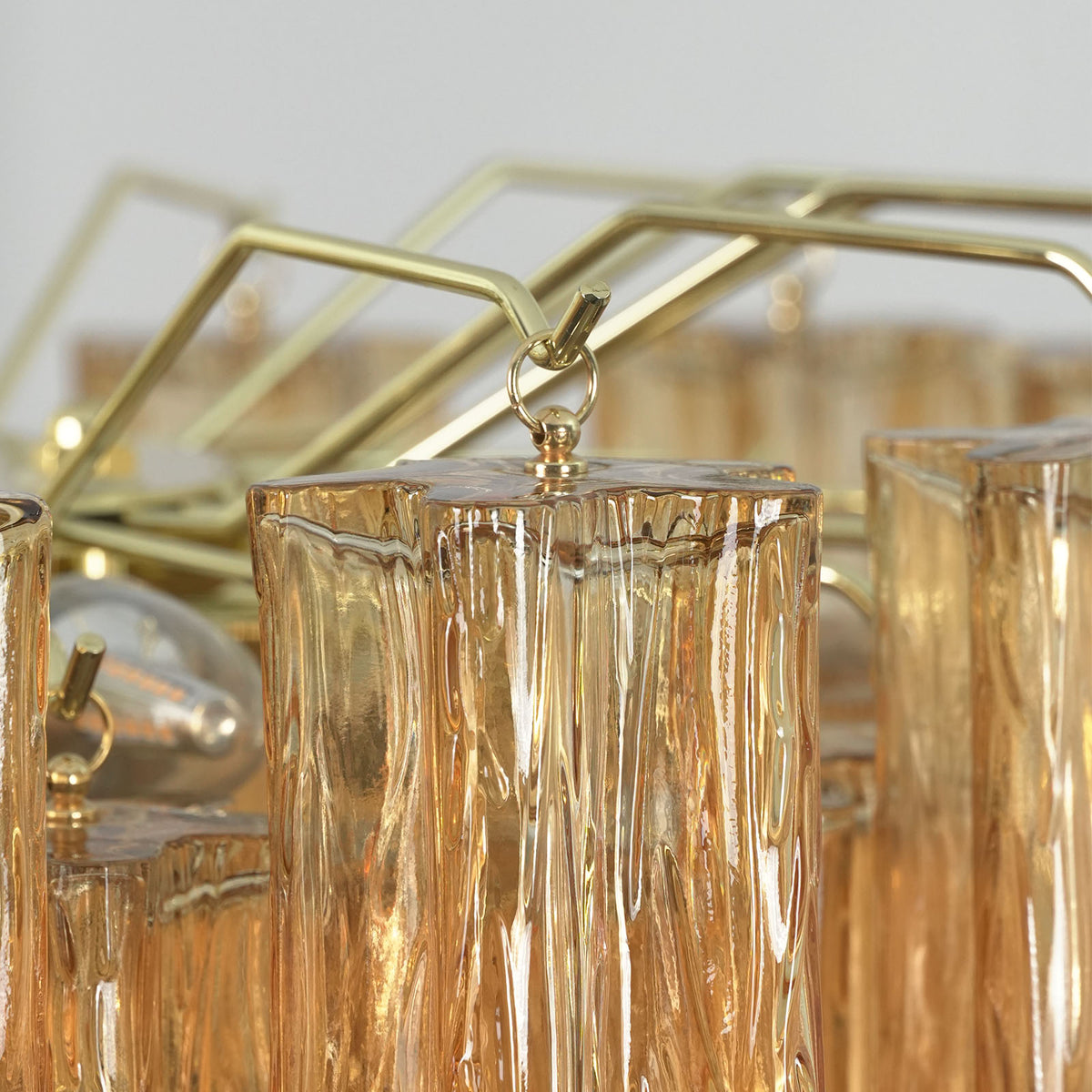 Merlande Amber Glass Tube Tiered Chandelier | Fluted Amber Glass and Brass | Macro close-up shot of brass mounting hooks holding amber glass tubes | Severn Lighting