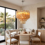 Merlande Amber Glass Tube Tiered Chandelier | Fluted Amber Glass and Brass | Suspended above a round dining table with light wood chairs near large windows | Severn Lighting