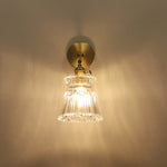 Merrick Fluted Glass Bell Wall Lamp | Fluted Glass and Brass | Front illuminated view showing warm light reflection on a dark backdrop | Severn Lighting