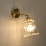 Merrick Fluted Glass Bell Wall Lamp | Fluted Glass and Brass | Angled illuminated view displayed against a dark studio background | Severn Lighting