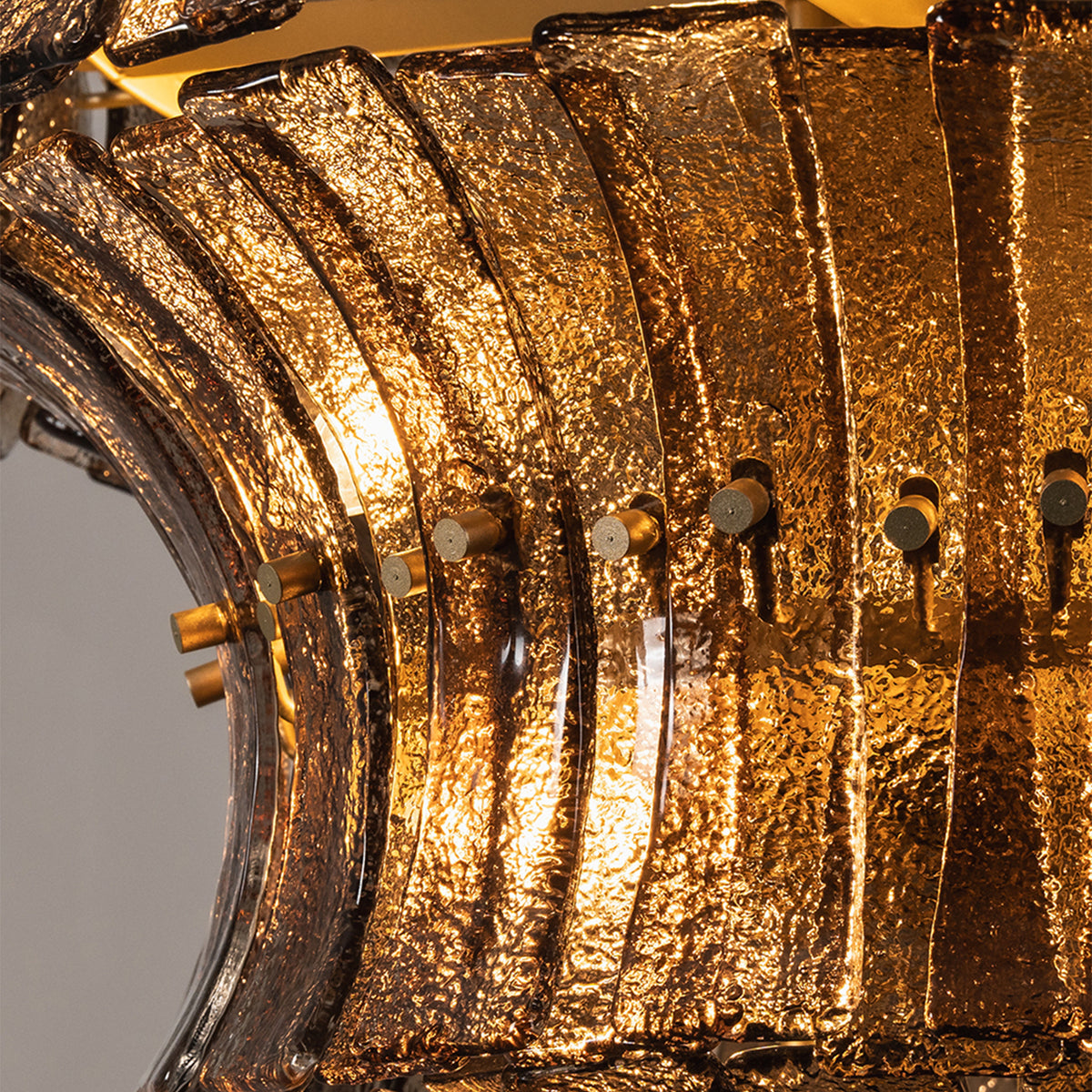 Octavia Sculptural Smoked Glass Chandelier | Textured Smoked Glass | Macro detail of the warm amber light filtering through overlapping textured glass tiers | Severn Lighting