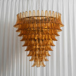 Odile Amber Petal Tier Chandelier | Amber Glass and Metal | Full illuminated view hanging against a white fluted wall panel | Severn Lighting