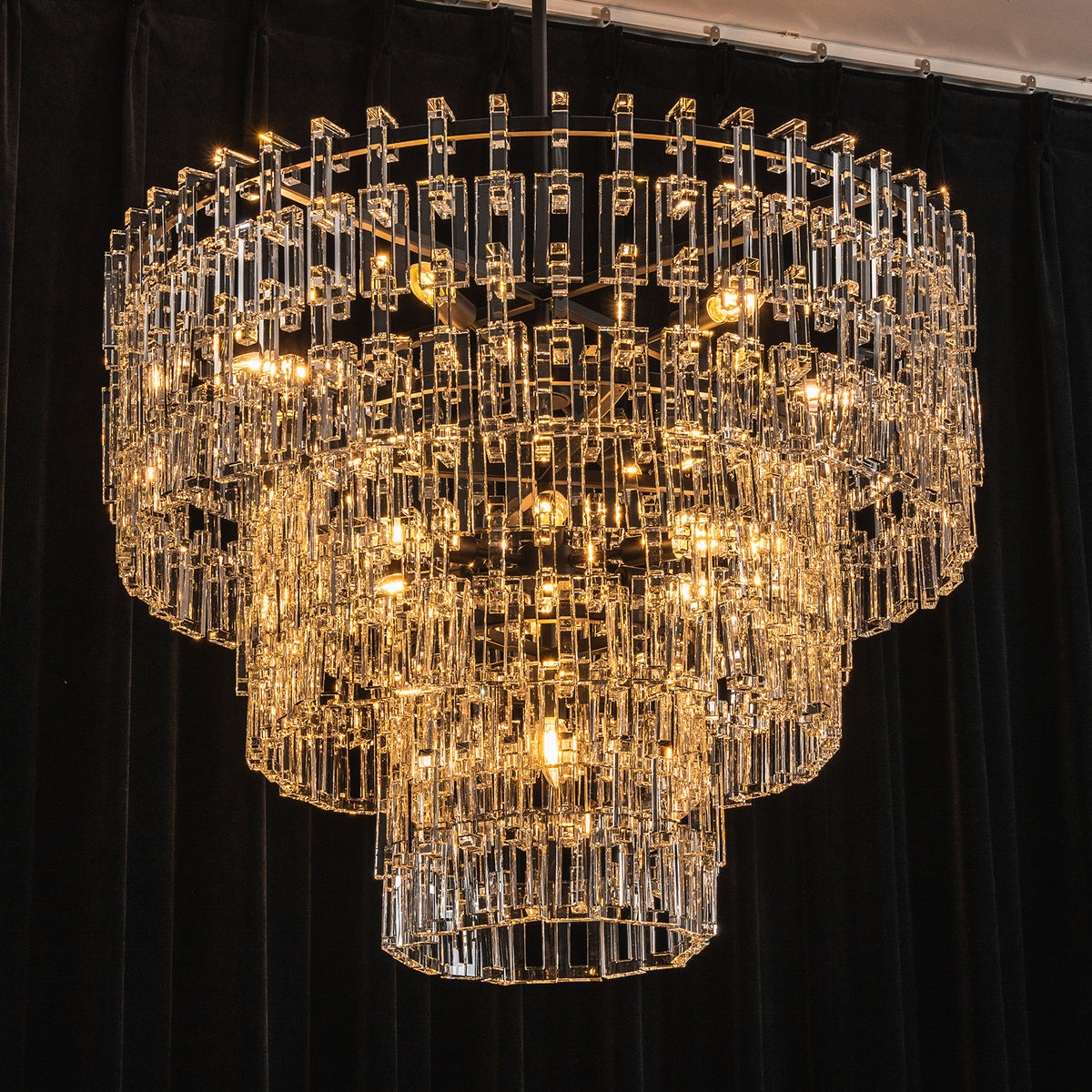 Rainer Cascading Glass Rod Chandelier | Clear Glass and Black Metal | Full view glowing brightly against a dark black backdrop | Severn Lighting