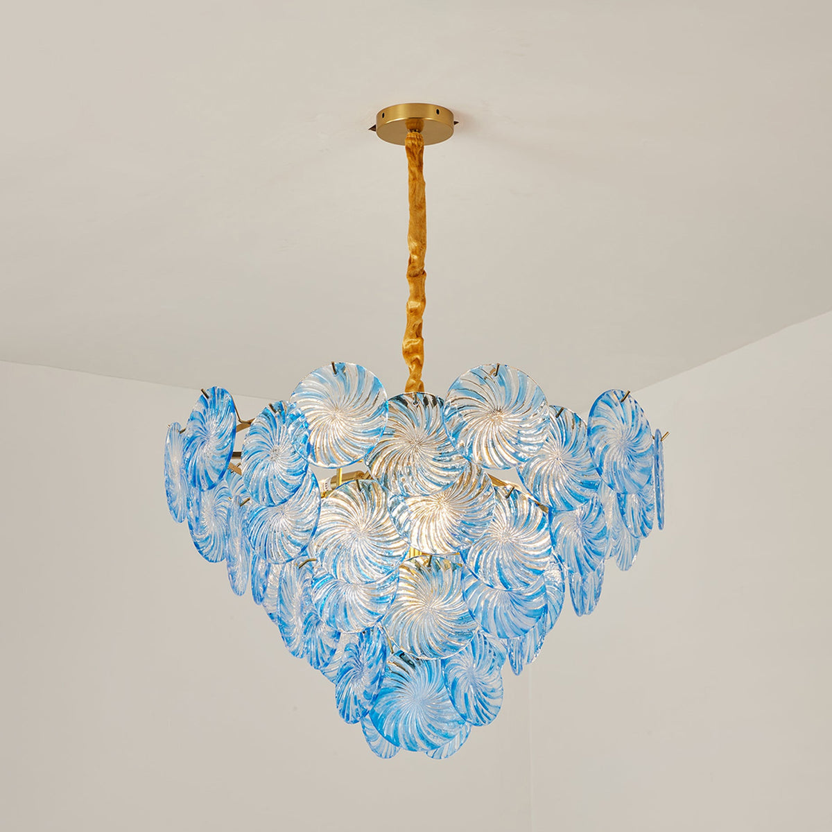 Rosalind Petal Glass Chandelier | Textured Spiral Blue Glass and Gold Metal | Minimalist view of the glowing blue chandelier hanging from a plaster ceiling in a room | Severn Lighting