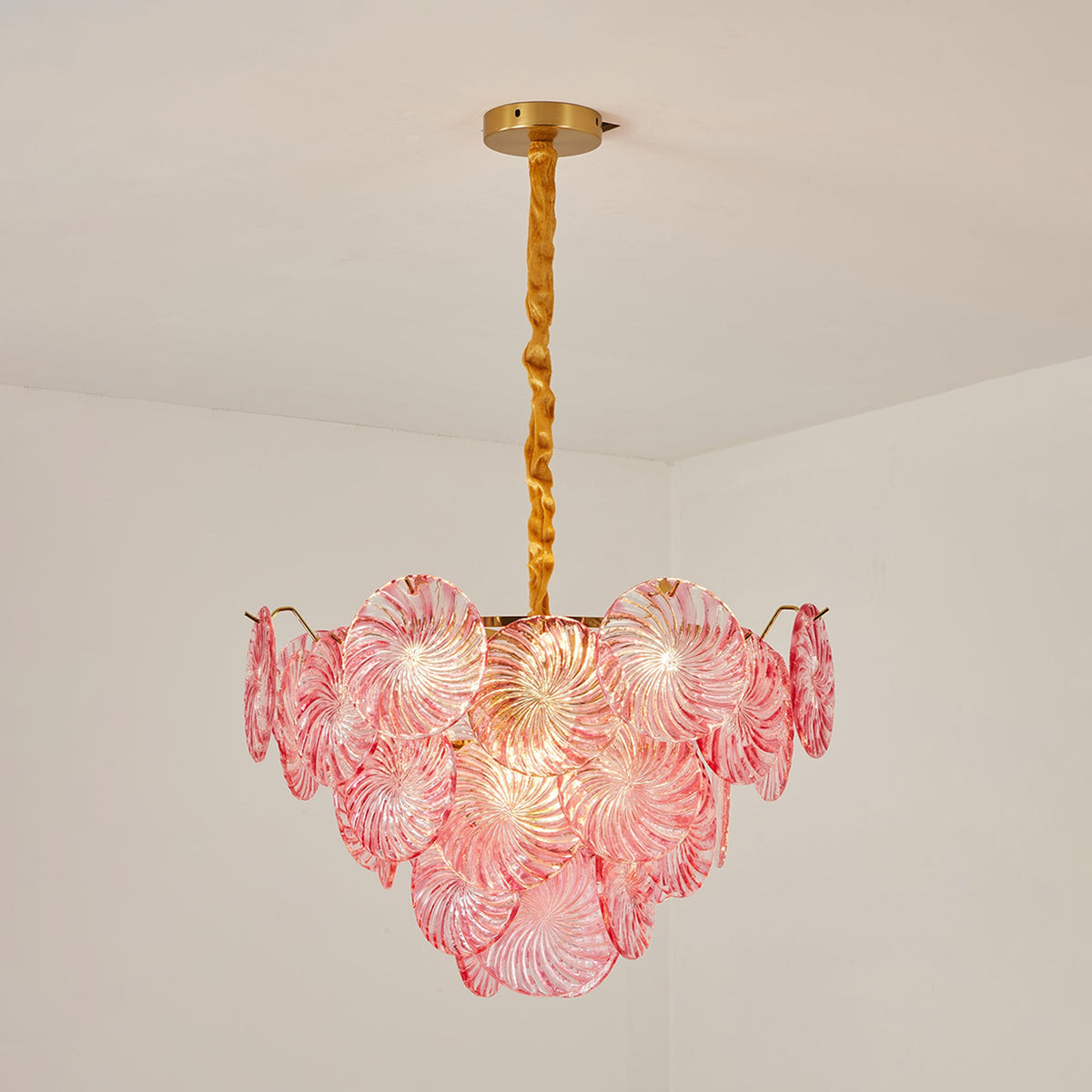 Rosalind Petal Glass Chandelier | Textured Spiral Pink Glass and Gold Metal | Standard product shot of the lit pink tiered fixture hanging from a gold chain on a white wall | Severn Lighting