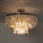 Sirena Capiz Disc Tiered Ceiling Light | Shell, Metal | Full view of the tiered shell chandelier lit up brilliantly against a moody dark studio background | Isolated shot | Samu Lamp