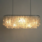 Sirena Capiz Elongated Linear Chandelier | Capiz Shell, Metal | Frontal view of the fully lit linear chandelier against a grey studio backdrop, showcasing the warm illumination | Samu Lamp