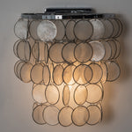 Sirena Capiz Tiered Wall Sconce | Capiz Shell, Metal | Front view of the fully lit cascading shell wall sconce radiating a warm golden glow against a neutral studio background | Samu Lamp