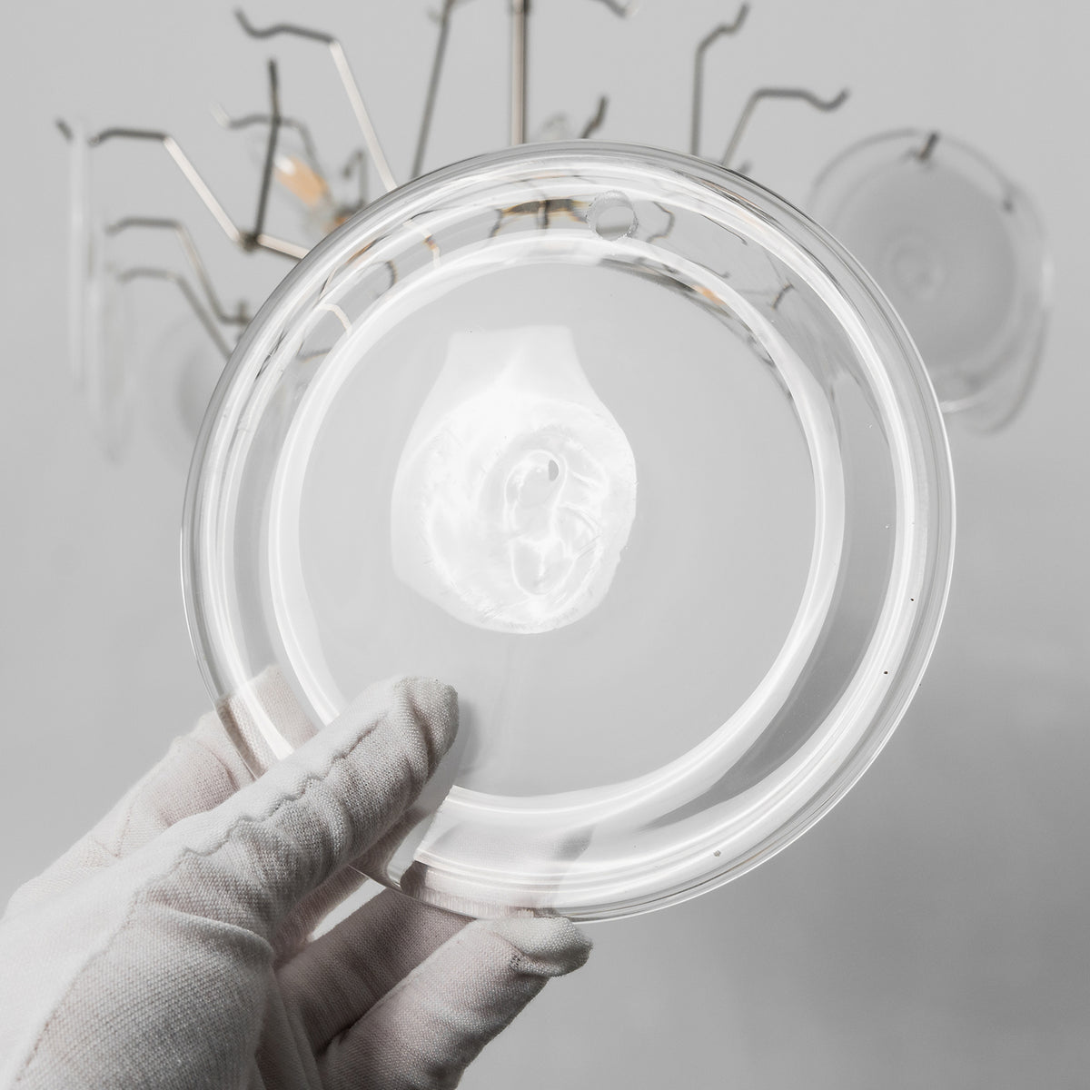 Solene Clustered Glass Disc Ceiling Light | Clear and Frosted Glass Discs | A hand wearing a white glove holding a single textured translucent circular glass plate component | Severn Lighting