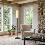 Stellan Alabaster Column Floor Lamp | Natural Alabaster, Brass and Black Metal | Illuminating a rustic living room with a fireplace and armchair | Severn Lighting