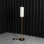 Stellan Alabaster Column Floor Lamp | Natural Alabaster, Brass and Black Metal | Illuminated full view displayed against a dark curtain backdrop | Severn Lighting