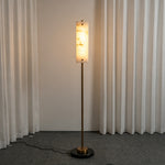 Stellan Alabaster Column Floor Lamp | Natural Alabaster, Brass and Black Metal | Full standing view glowing softly against textured white drapes | Severn Lighting