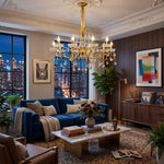 Torvald Scrolled Crystal Brass Chandelier | Cut Crystal and Brass | Illuminating a modern living room at night with a blue sofa and city view | Severn Lighting