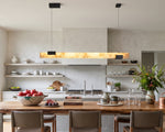 Vale Alabaster Linear Glow Pendant Lighting | Natural Alabaster and Black Metal | Suspended above a spacious wooden kitchen island counter with brown leather bar stools | Severn Lighting