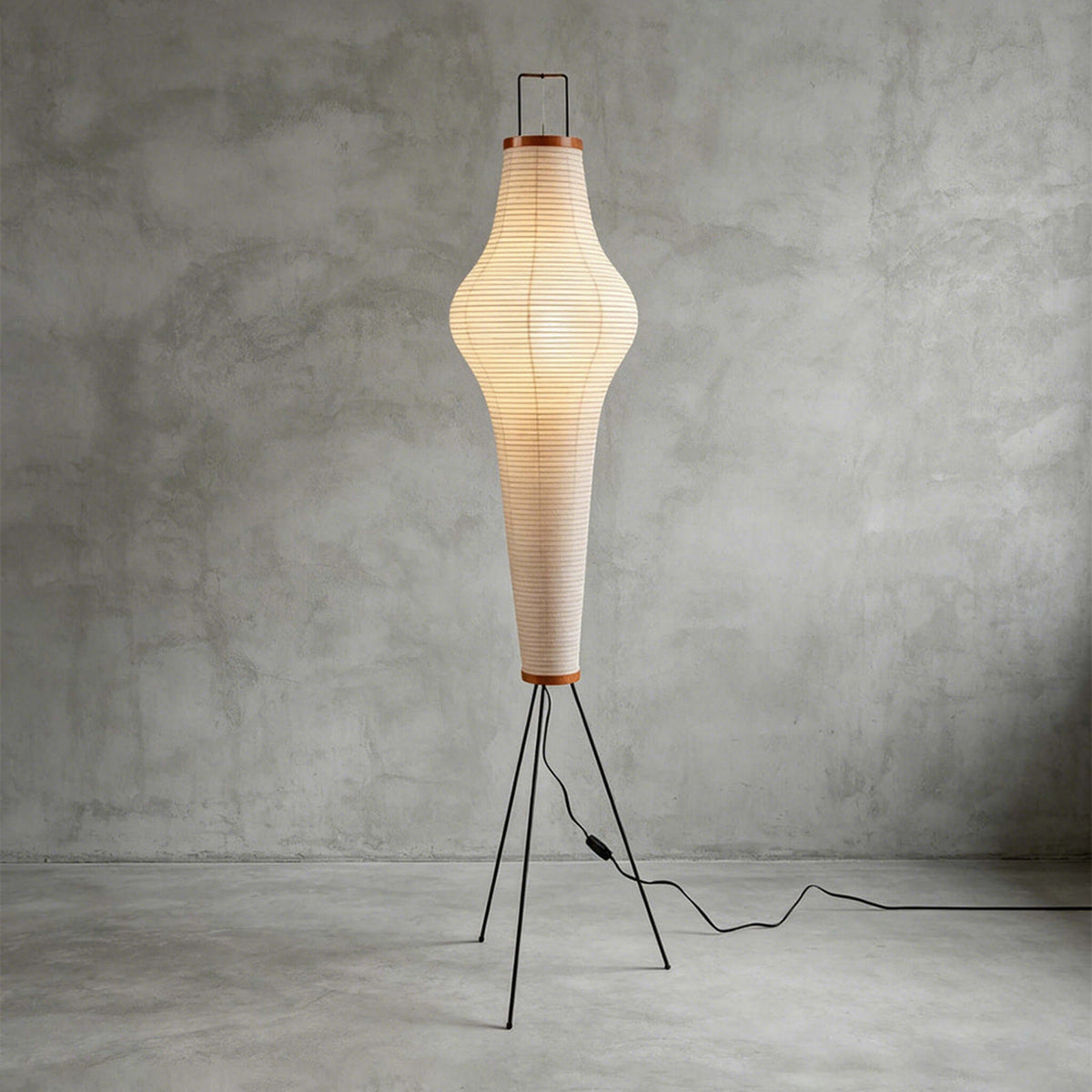Verena Ribbed Paper Column Floor Lamp | Ribbed Paper and Metal Tripod Legs | Full studio display against a rustic textured grey wall background with the column lamp fully lit | Severn Lighting