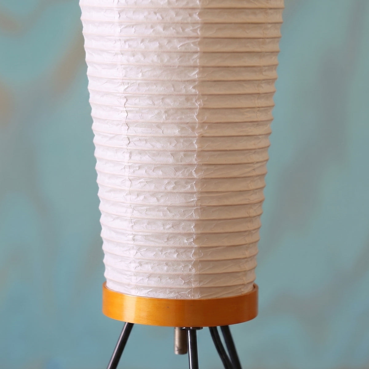 Verena Ribbed Paper Column Floor Lamp | Ribbed Paper and Metal Tripod Legs | Close-up of the lower section of the lamp highlighting the orange wooden rim connecting to the tripod base | Severn Lighting