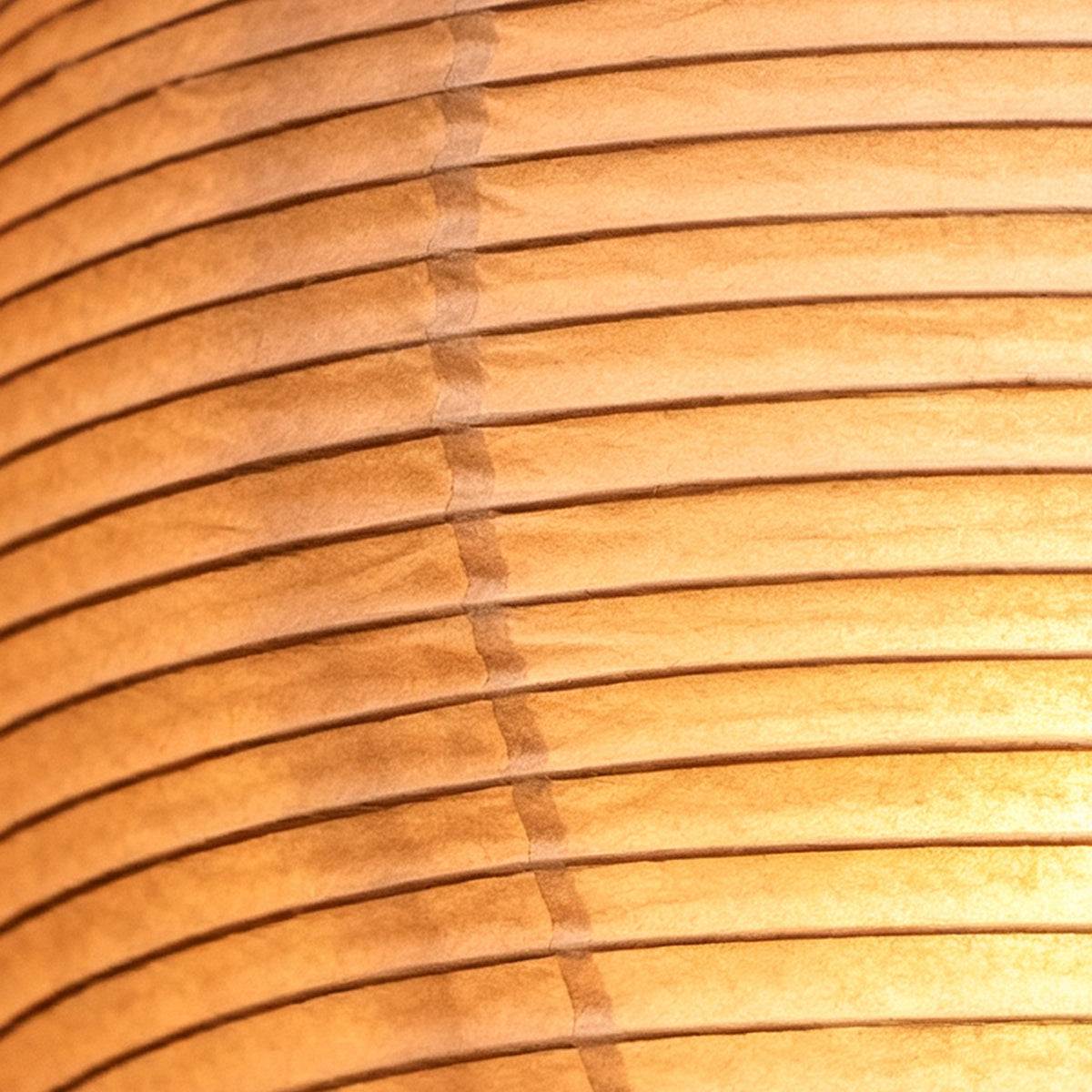 Verena Ribbed Paper Column Floor Lamp | Ribbed Paper and Metal Tripod Legs | Extreme close-up shot detailing the horizontal ribbed texture of the warm glowing paper lantern | Severn Lighting