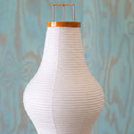 Verena Ribbed Paper Column Floor Lamp | Ribbed Paper and Metal Tripod Legs | Macro view of the white sculptural paper shade upper silhouette against a textured blue background | Severn Lighting