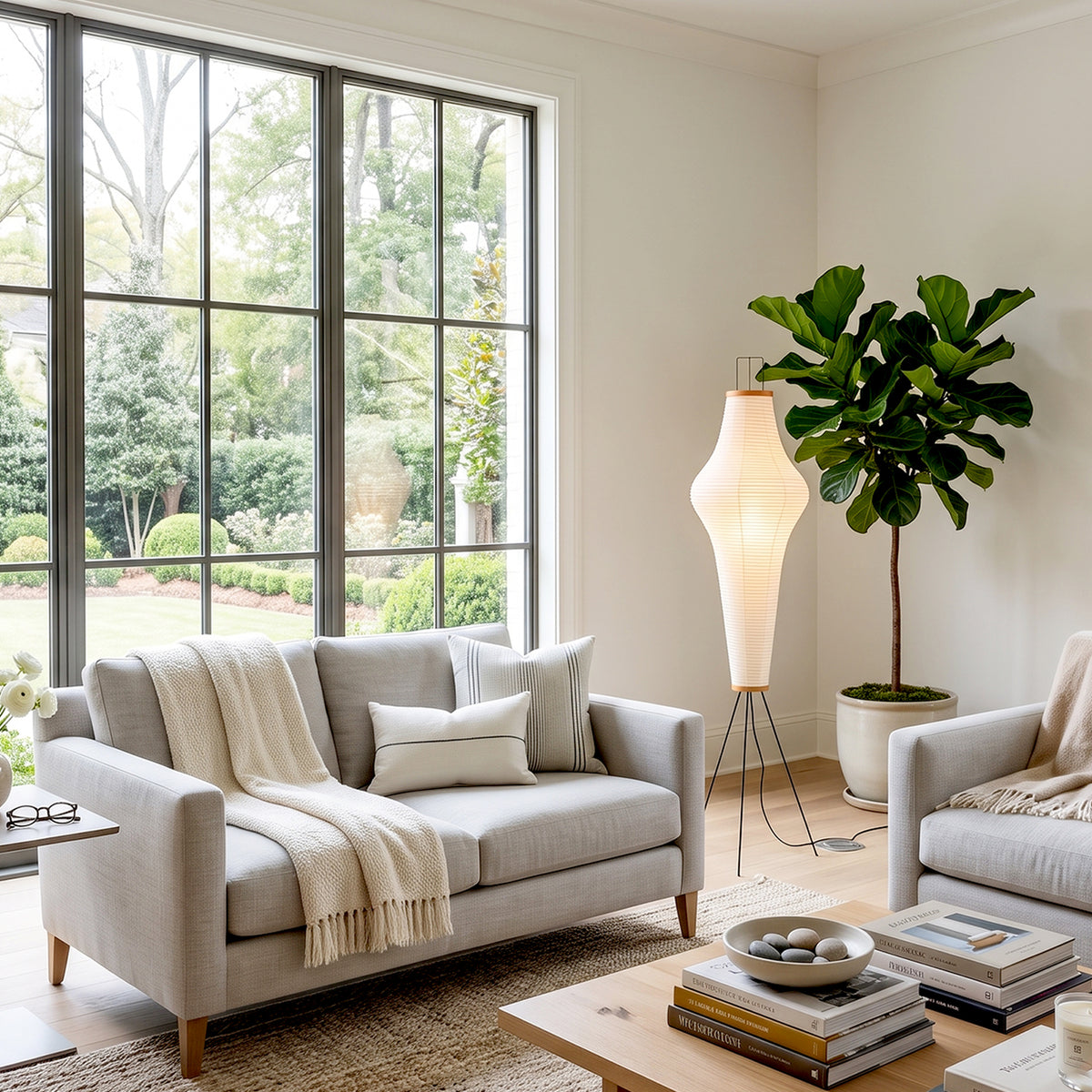 Verena Ribbed Paper Column Floor Lamp | Ribbed Paper and Metal Tripod Legs | Illuminating a modern contemporary living room next to a light grey fabric sofa and a potted tree | Severn Lighting